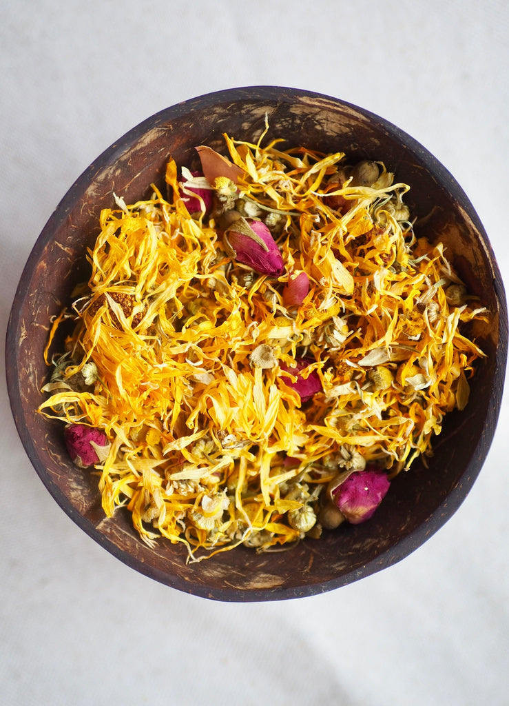 little koko sweet dreams baby massage oil dried rose petals, calendula and chamomile flowers in a coconut bowl