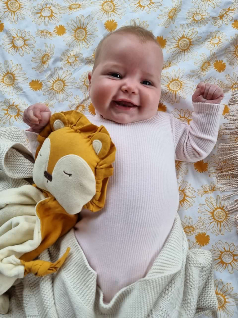 Happy baby with Little Koko Lion comforter, laying on a daisy blanket