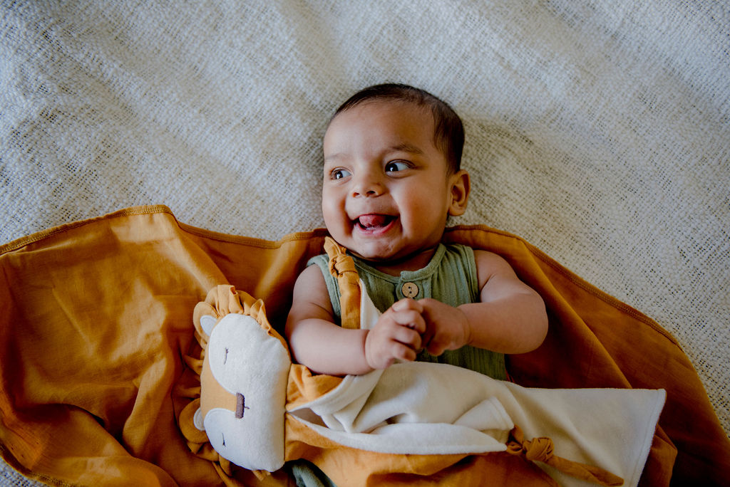 Baby lying on a textured surface with Little Koko Lion organic comforter, wearing a green outfit.