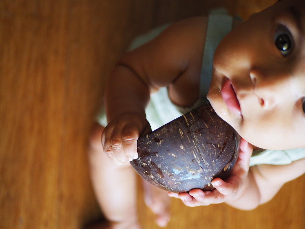 a baby holding a little koko bath time coconut shell used for play time