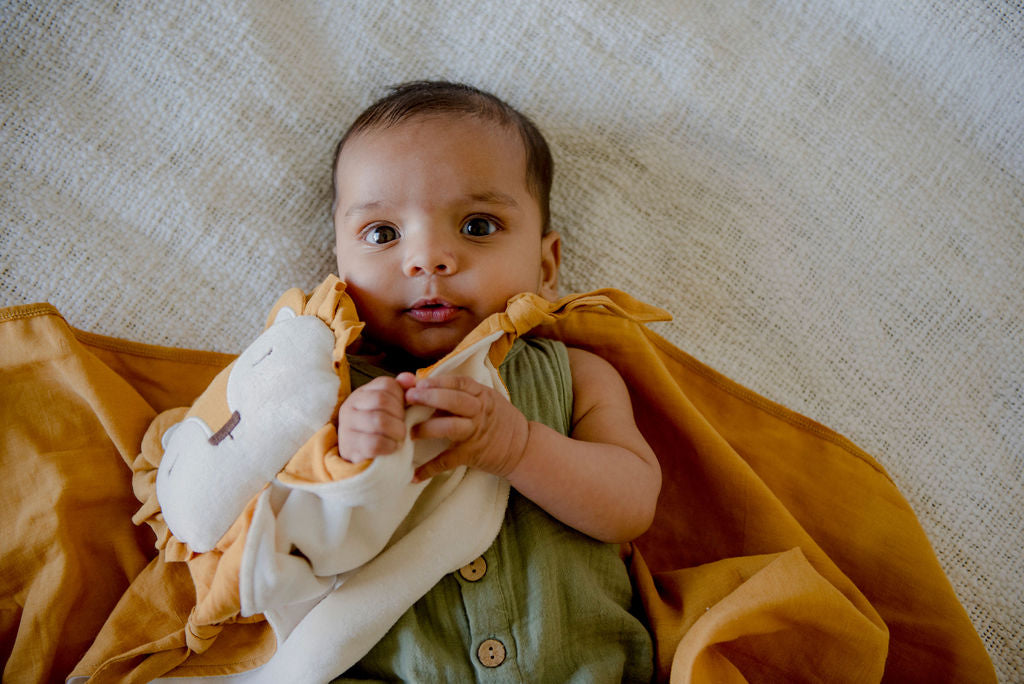 a baby laying on a little koko linen wrap holding a little koko lion comforter