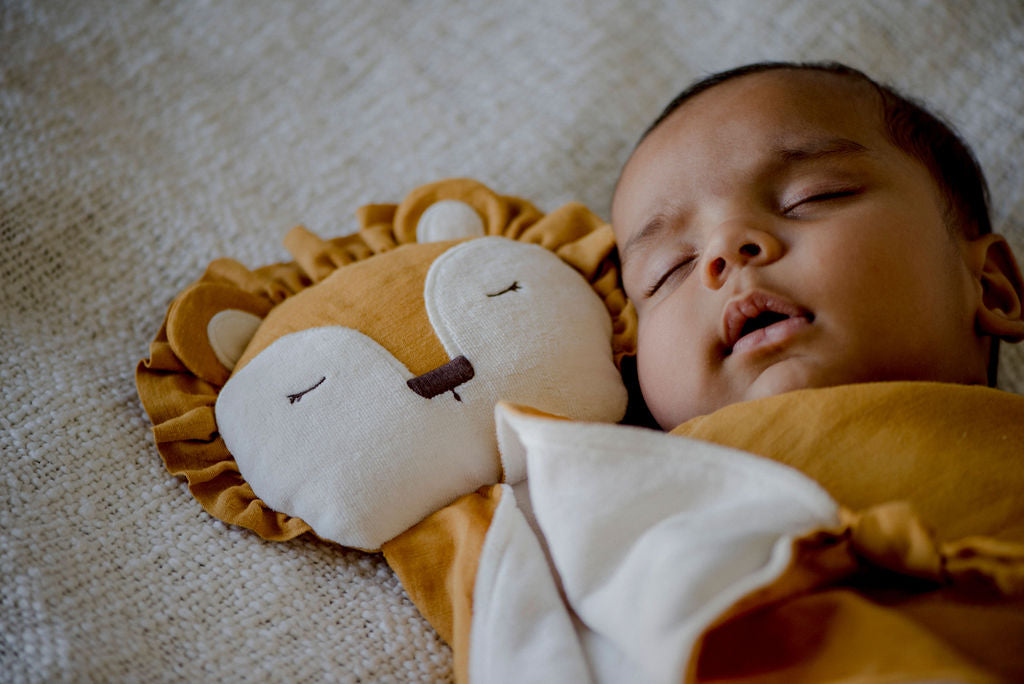 a baby sleeping with a little koko lion comforter