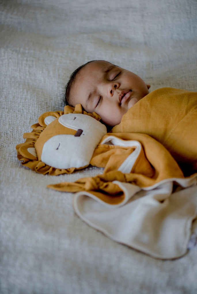 relaxed sleeping baby swaddled in a little koko linen wrap with a little koko lion comforter